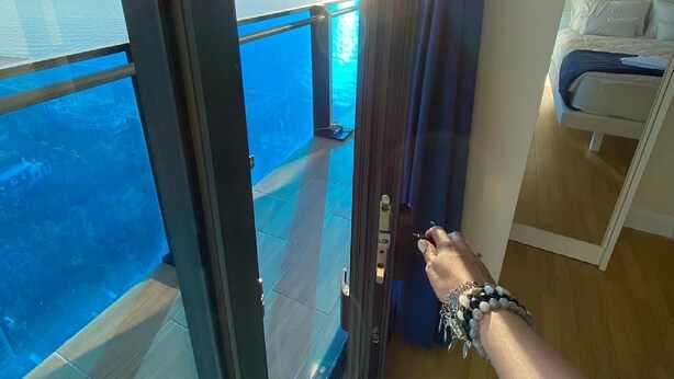 A room with a bed, a view of the ocean, and a door leading outside.