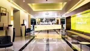 A modern hotel lobby with a reception desk, seating area, and a large digital display.