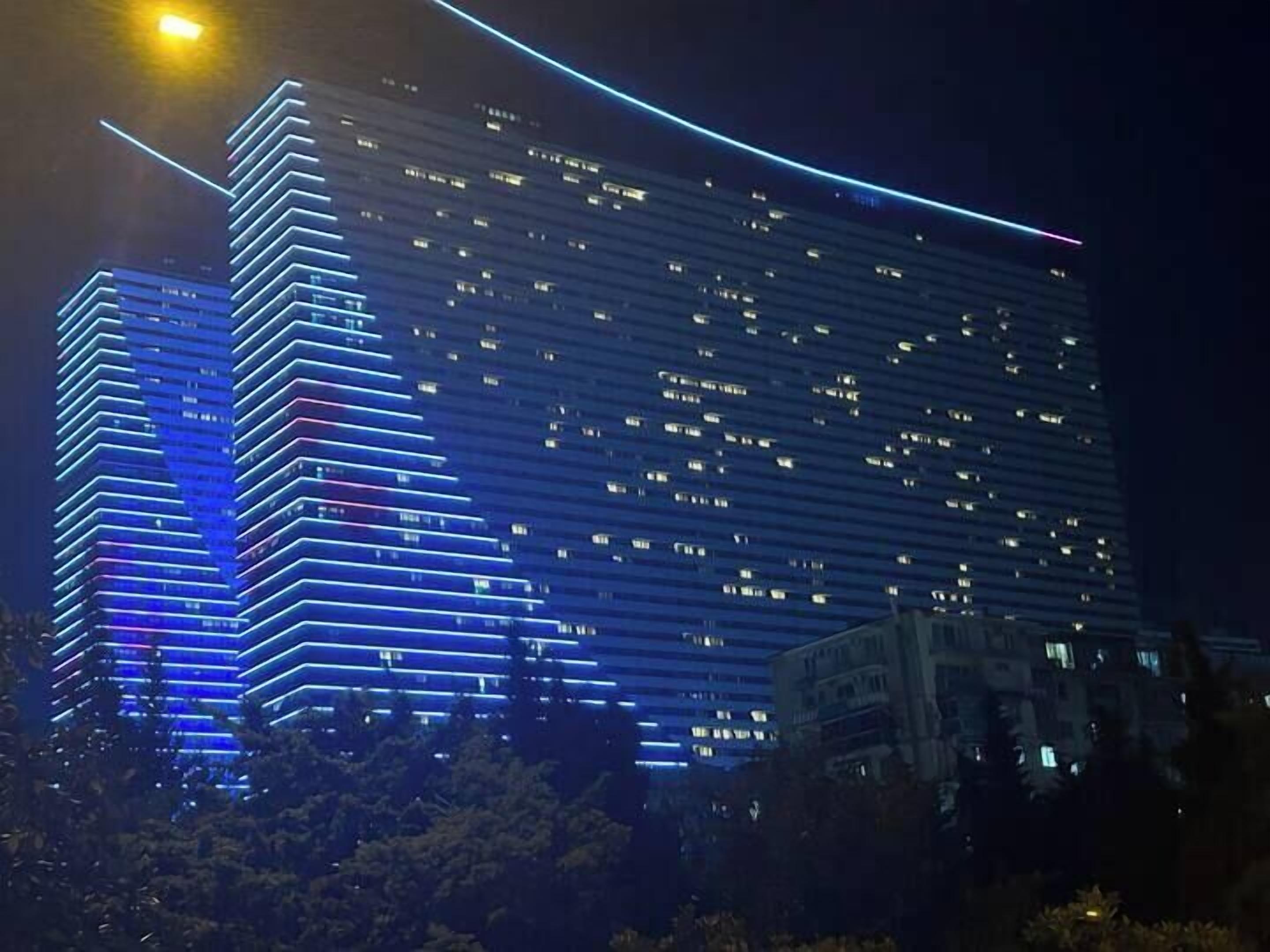 Un immeuble à étages doté d’une architecture moderne, caractérisé par des rangées horizontales de fenêtres et des contours illuminés.