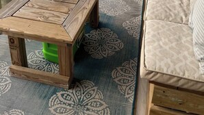 A wooden table with a coiled cable, a green stool, and a patterned rug on a balcony with a view of the ocean. - 3 bedroom condo on the 12th floor in beautiful Panama City Beach (Panama City Beach)