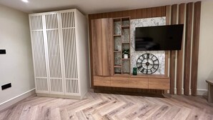 Ein modernes Wohnzimmer mit einem Fischgrätparkettboden, einem integrierten Fernseher, einer Holzeinbauvitrine mit Regalen und einer Wand mit Marmorverkleidung.