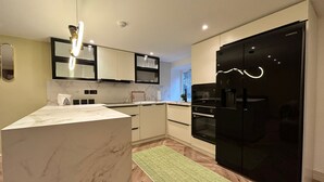 Eine moderne Küche mit Marmorarbeitsplatte, eingebauten Geräten und einem schwarzen Kühlschrank.