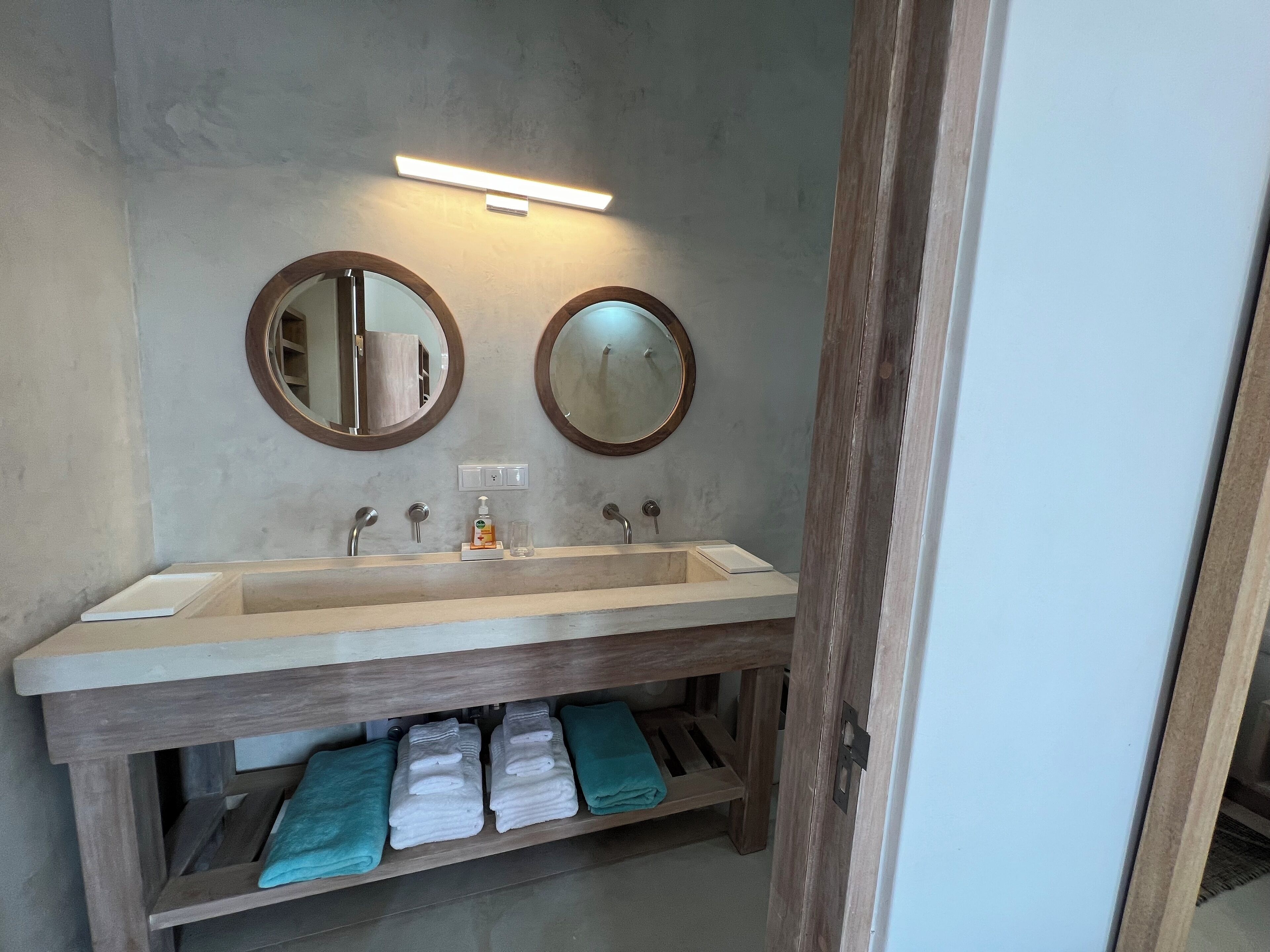 A bathroom with a large sink, two mirrors, and a towel rack with folded towels.