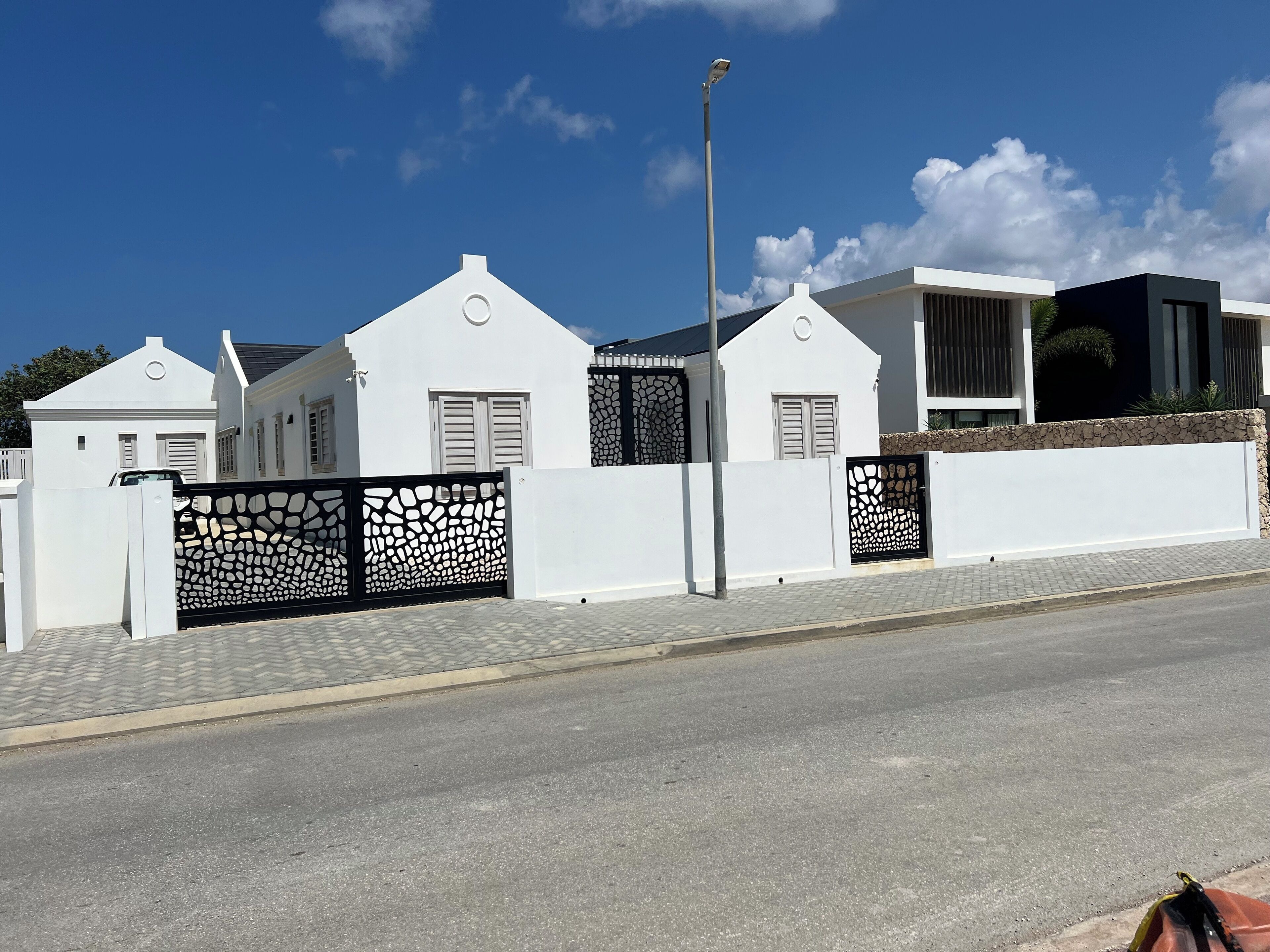 A modern white house with a stone wall and decorative black gates.