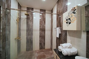 Bathroom features a glass-enclosed shower area with a showerhead and control panel, surrounded by a mix of brown and white tiles.