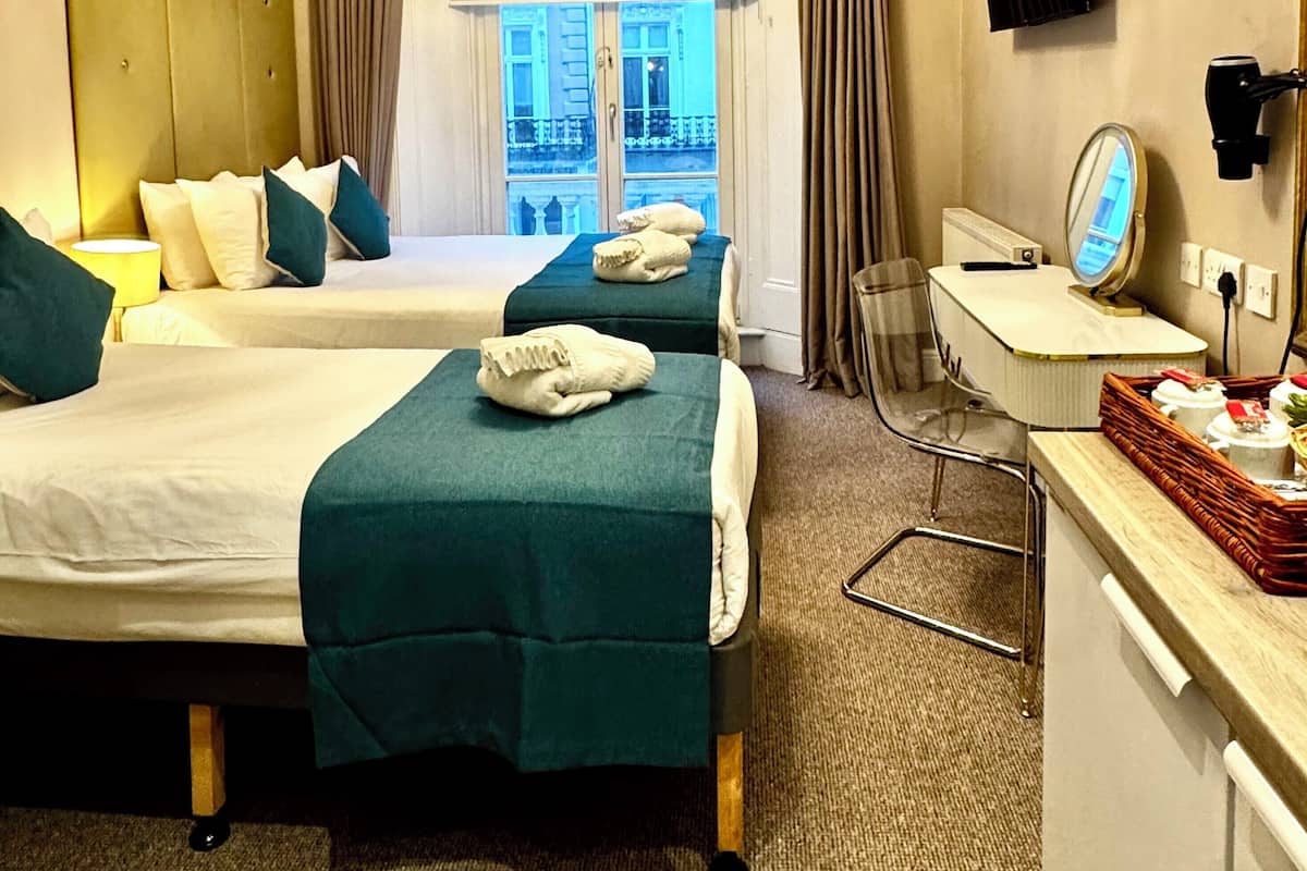 A hotel room with two beds, a desk, a chair, a TV, and a large window with curtains.
