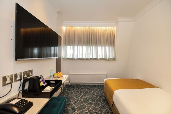Une chambre d’hôtel comprenant un lit, un bureau avec un téléphone, une machine à café, un radiateur et une fenêtre avec des rideaux.