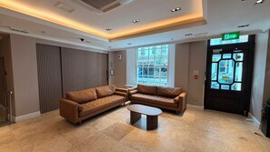 A modern lobby with a sectional sofa, a coffee table, and a large window providing a view of the outside. - Queens Park Premier London Hyde Park (London)