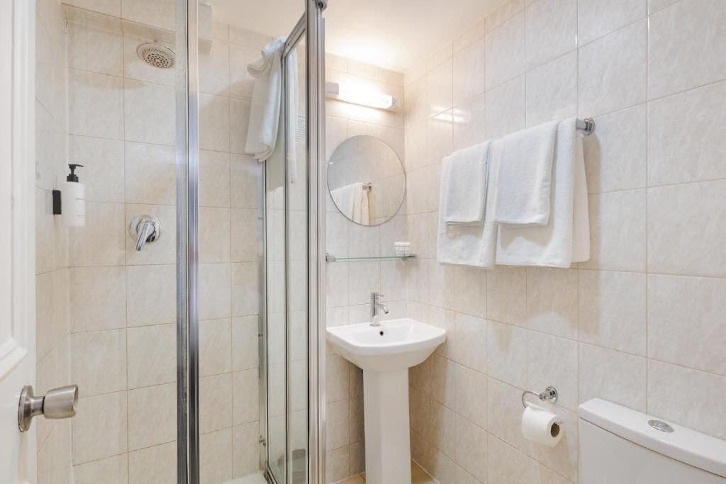 Une salle de bain moderne avec une douche à parois de verre, un lavabo sur colonne, un miroir rond et des toilettes.