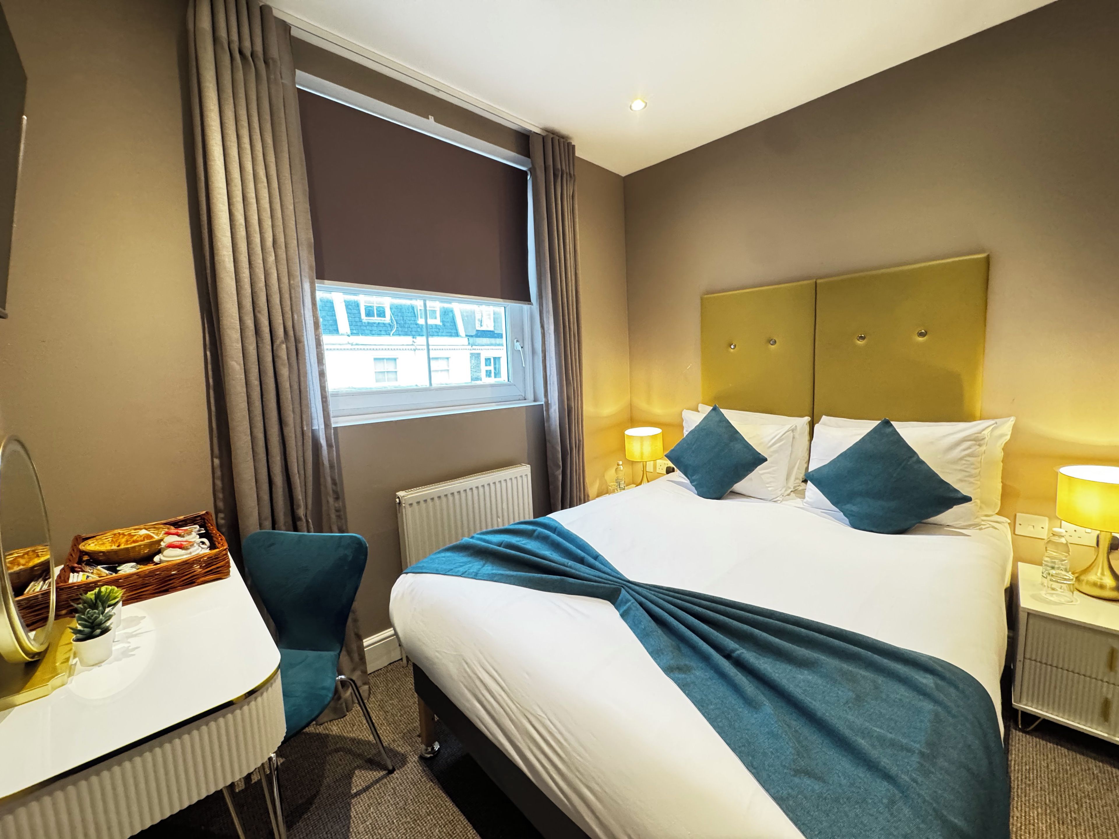 A hotel room with a bed, bedside tables, a desk, and a window with curtains.