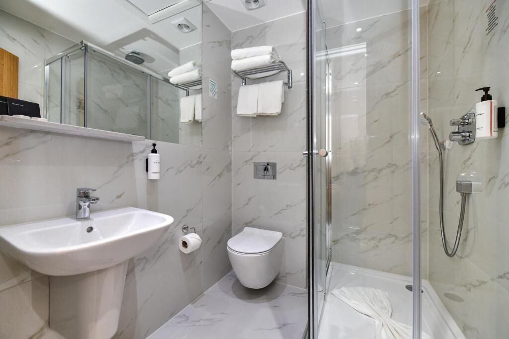 A modern bathroom with a glass-enclosed shower, a white sink, and a toilet.