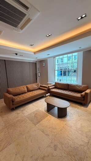 A modern living room with two sofas, a coffee table, and a large window providing a view of the outside. - Queens Park Premier London Hyde Park (London)