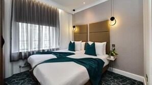 Hotelkamer met twee bedden, een groot raam met gordijnen, een hoofdbord met geïntegreerde verlichting en een klein nachtkastje met een plantje.