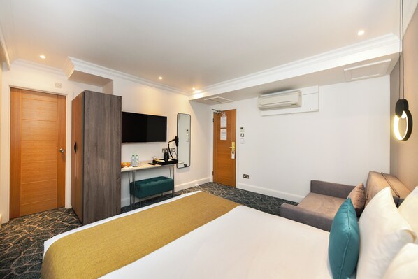 A hotel room with a large bed, a desk with a chair, a television, and a wardrobe.