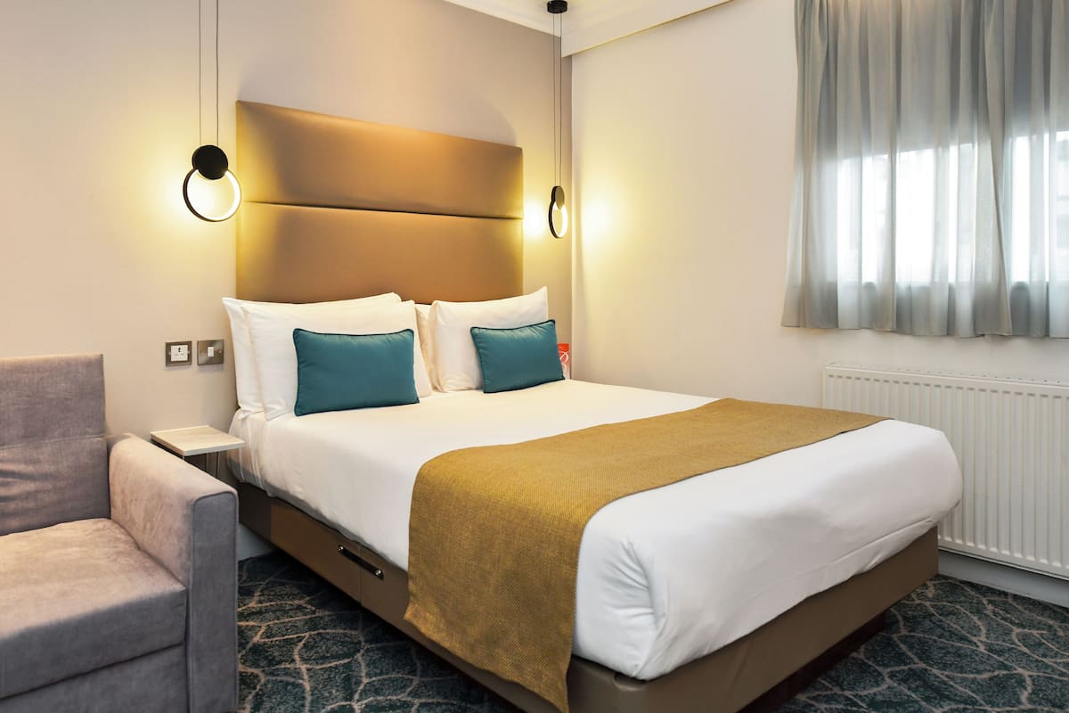 A hotel room with a bed, a nightstand, a chair, and a window with curtains.