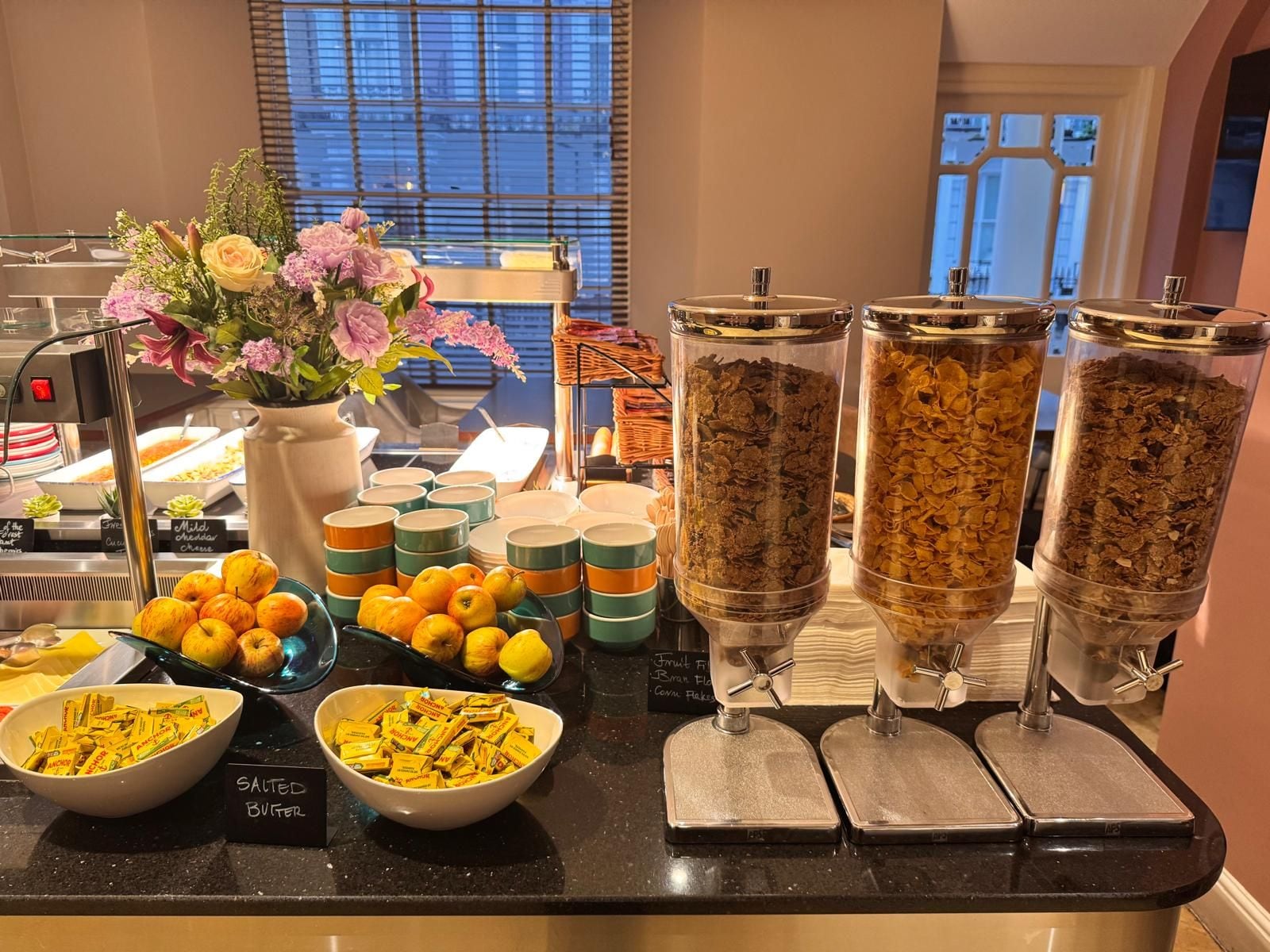 A buffet setup with various food items, including fruits, cereals, and condiments.