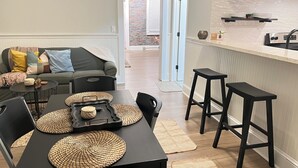 A modern kitchen with a dining area, featuring a black table with woven placemats, a black bar stool, and a black chair. - Stunning Loft  from 1860 in Frechtown St Charles Mo (Saint Charles)