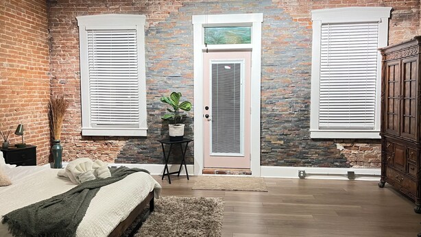 A bedroom with a brick wall, a bed with a green blanket, a small table with a plant, and a wooden cabinet. - Stunning Loft  from 1860 in Frechtown St Charles Mo (Saint Charles)