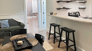 A modern kitchen with a white countertop, black stools, and a dining area with a table and chairs. - Stunning Loft  from 1860 in Frechtown St Charles Mo (Saint Charles)