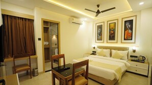 A hotel room with a bed, bedside tables, a desk with chairs, a ceiling fan, and artwork on the walls. - Wishotel Premier The Phoenix Hotel 2.O (Indore)