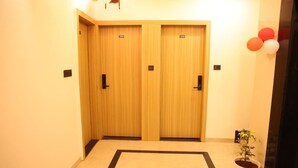 A hallway with two wooden doors, each marked with a number. There is a potted plant on the right side. - Wishotel Premier The Phoenix Hotel 2.O (Indore)