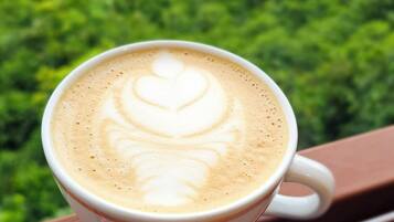 Una taza de café con arte de latte en un balcón con vistas a un paisaje verde exuberante.