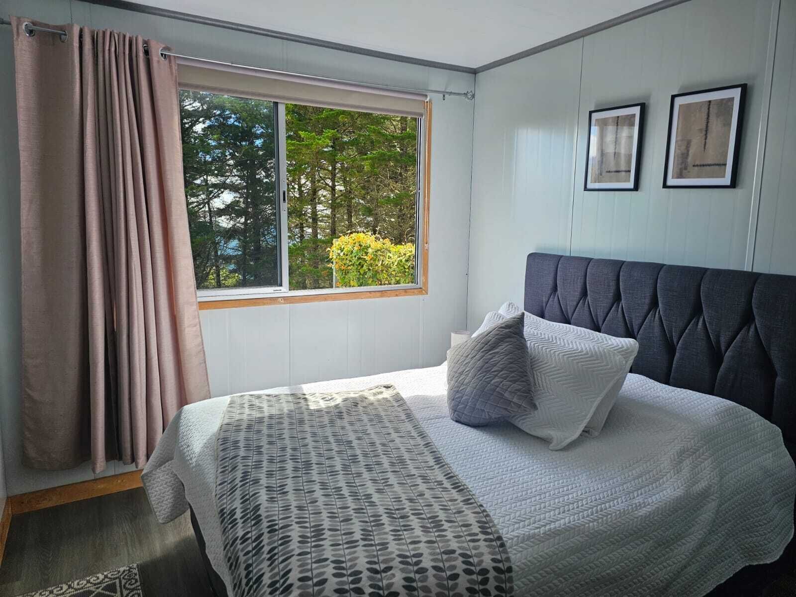 A bedroom with a bed, a window with curtains, and framed pictures on the wall.
