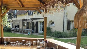 Un área de bar al aire libre con madera, un lavamanos, vasos y una lámpara colgante.