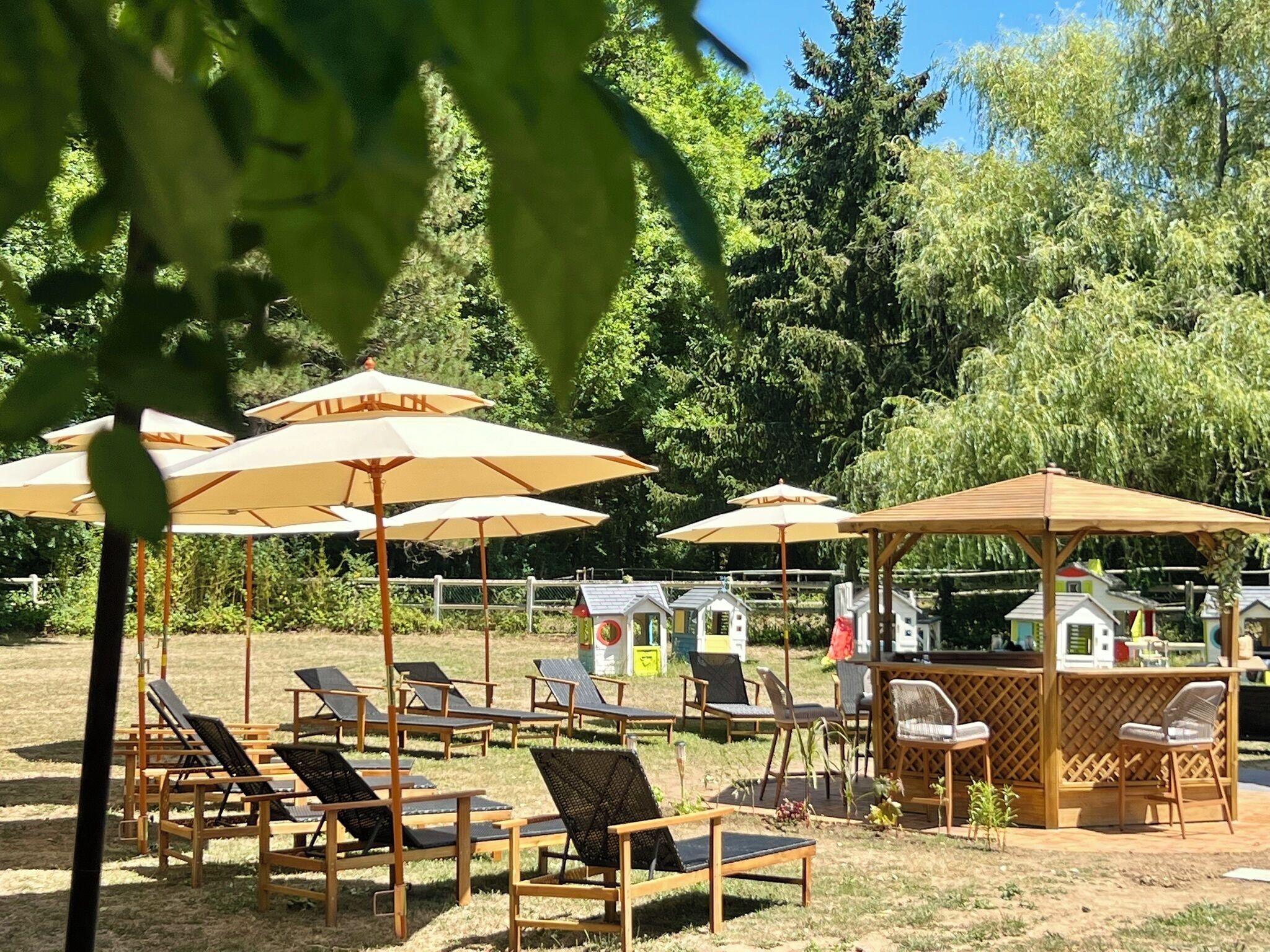 A beachside area with sun loungers and umbrellas, a wooden gazebo, and a fenced playground.