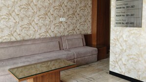 Une pièce avec un mur décoré d’un motif imitant le marbre, un canapé beige et une table avec un plateau en verre. Un panneau indique les numéros des chambres pour les différents étages.