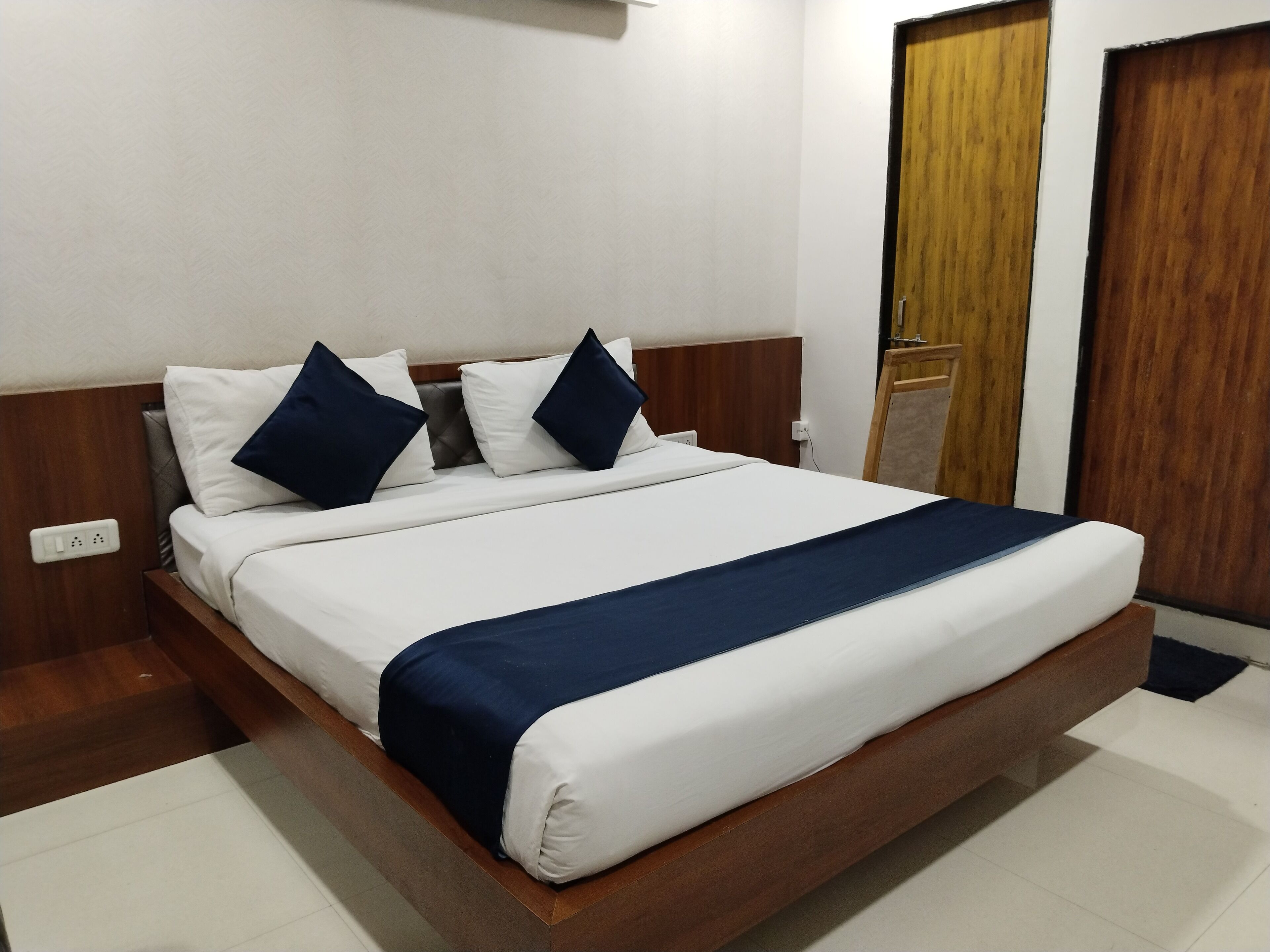 A neatly made bed with white and navy bedding, a wooden headboard, and a wooden floor.