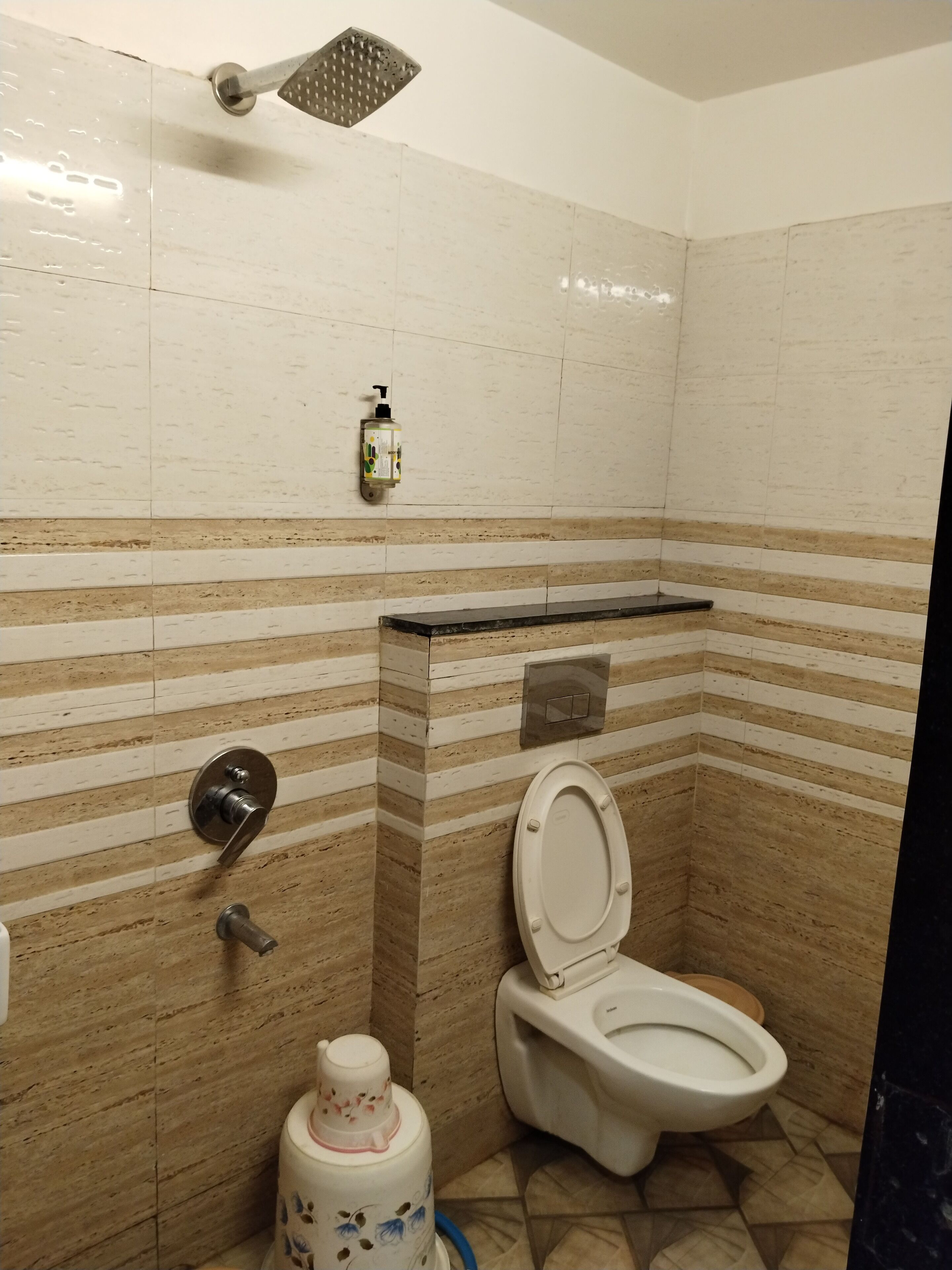 A bathroom with a toilet, a hand dryer, a soap dispenser, and a trash bin.