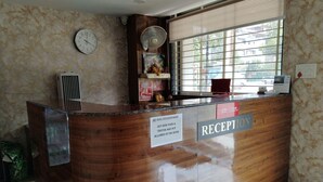 Un comptoir d’accueil d’hôtel avec une horloge, une fenêtre avec des stores et un panneau indiquant l’emplacement de la réception.
