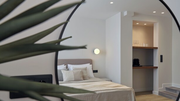 Una camera da letto con un letto, un comodino e una lampada da notte. Sopra il letto c'è una luce fissata al muro e una porta che dà su un bagno.