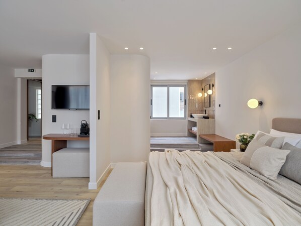 A modern bedroom with a large bed, a TV, and a bathroom with a vanity. - Haya Athens Loftie Suites (Athens)