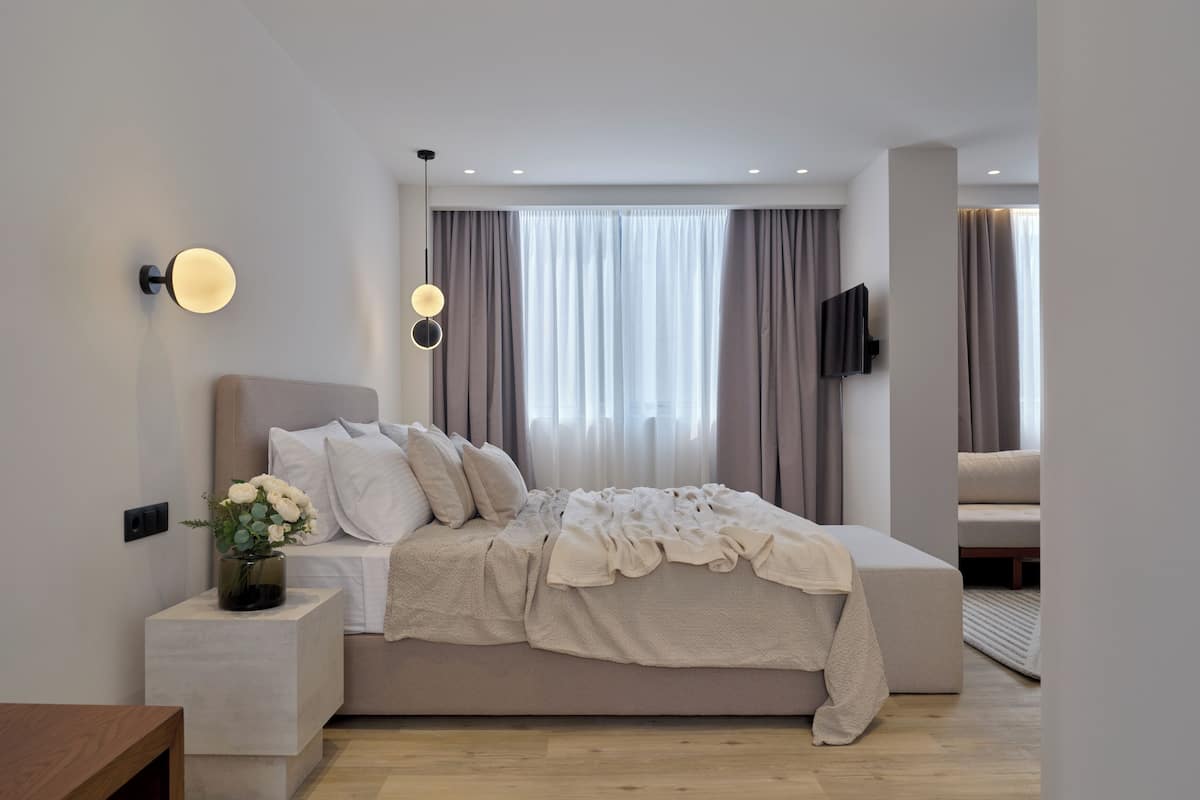 A modern bedroom with a large bed, bedside tables, a wall-mounted TV, and a window with curtains.