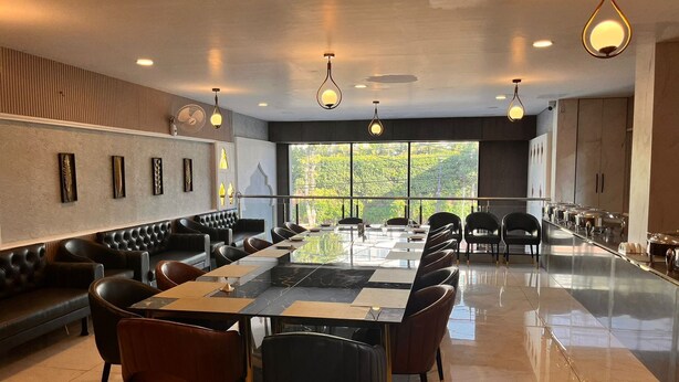 A modern dining area with a long table, black leather seating, and pendant lighting. - Wishotel Inn Skymoon  (Indore)
