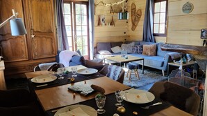 L’intérieur chaleureux d’un chalet avec des murs en bois, un coin repas agrémenté d’assiettes, de verres et de couverts, et un espace de détente avec un canapé et un téléviseur.