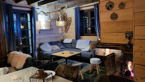 L’intérieur chaleureux d’un chalet avec un canapé, une petite table, une cheminée et des murs en bois.