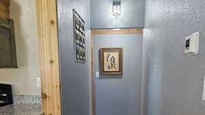 A narrow hallway with wooden flooring and a gray wall. There is a framed picture on the wall and a light fixture above it. - Relax in the wilderness at Bowie Acres (Bowie)