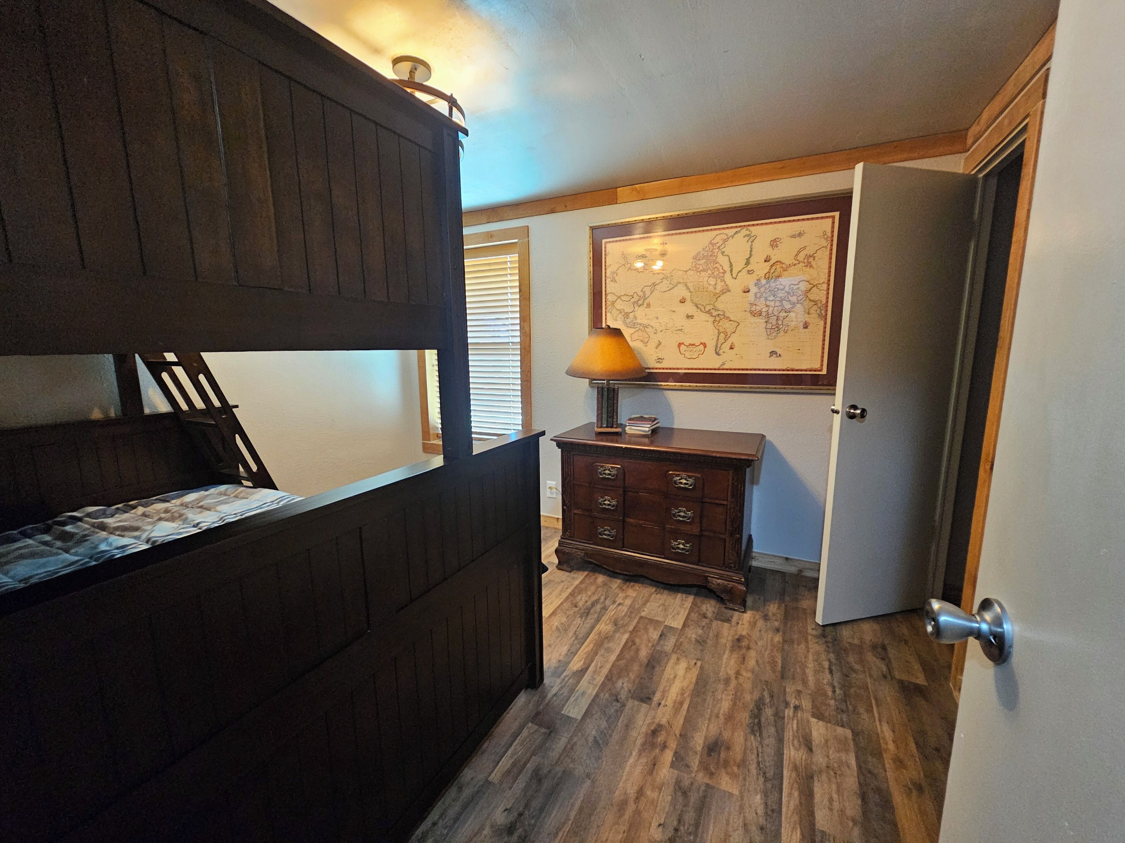 Een kamer met een stapelbed, een dressoir, een kaart aan de muur en een deur.
