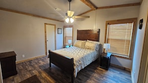A bedroom with a wooden bed, a ceiling fan, a window with blinds, and a nightstand with a lamp. - Relax in the wilderness at Bowie Acres (Bowie)