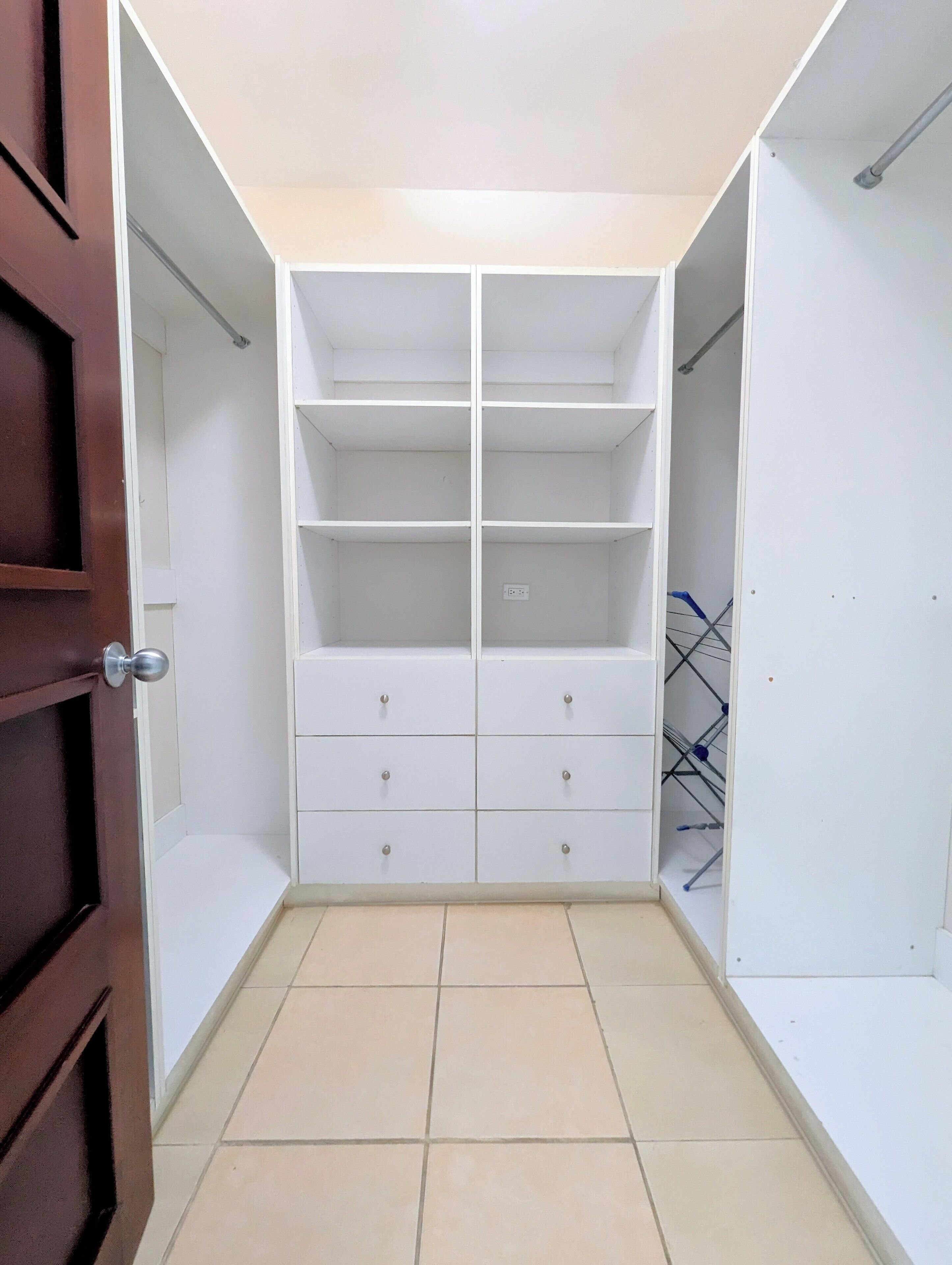 Un dressing accessible sans porte, doté d’étagères et de tiroirs ouverts, d’un sol carrelé et d’une tringle métallique pour suspendre les vêtements.