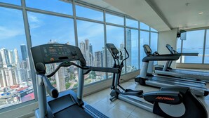 Un gimnasio con grandes ventanales que ofrecen vistas a la ciudad, equipado con máquinas de cardio como cintas de correr y elípticas.