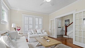 A spacious living room with a white sofa, a wooden coffee table, and a large window with shutters. - Spacious Home Walk to Historic DT w/Yard, Bikes (Saint Augustine)