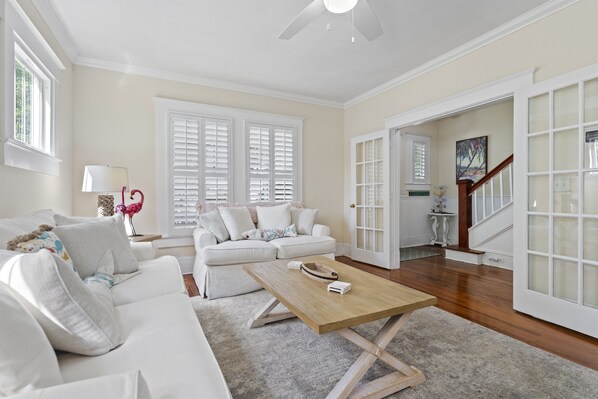 Un salón espacioso con un sofá blanco, una mesa de centro de madera y un ventanal con contraventanas.