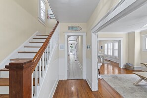 Un pasillo con escalera de madera, paredes blancas y vista a otra habitación.