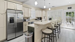 A modern kitchen with a stainless steel refrigerator, a built-in water dispenser, a coffee maker, and a large island with bar stools. - Spacious Home Walk to Historic DT w/Yard, Bikes (Saint Augustine)