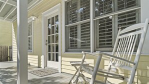 A porch with a rocking chair and a bench, a wooden door, and a window with blinds. - Spacious Home Walk to Historic DT w/Yard, Bikes (Saint Augustine)