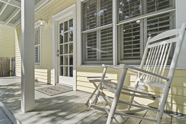 A porch with a rocking chair and a bench, a wooden door, and a window with blinds. - Spacious Home Walk to Historic DT w/Yard, Bikes (Saint Augustine)